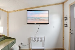 A room with a television mounted on the wall, a bed with a green headboard, a bedside table with a lamp, and a small white chair. - Lake Views, Private Dock, Paddle Boards & Bunk House (Gravois Mills)