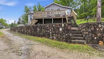 A house with a stone wall, a wooden deck, and a staircase leading to a second floor.
