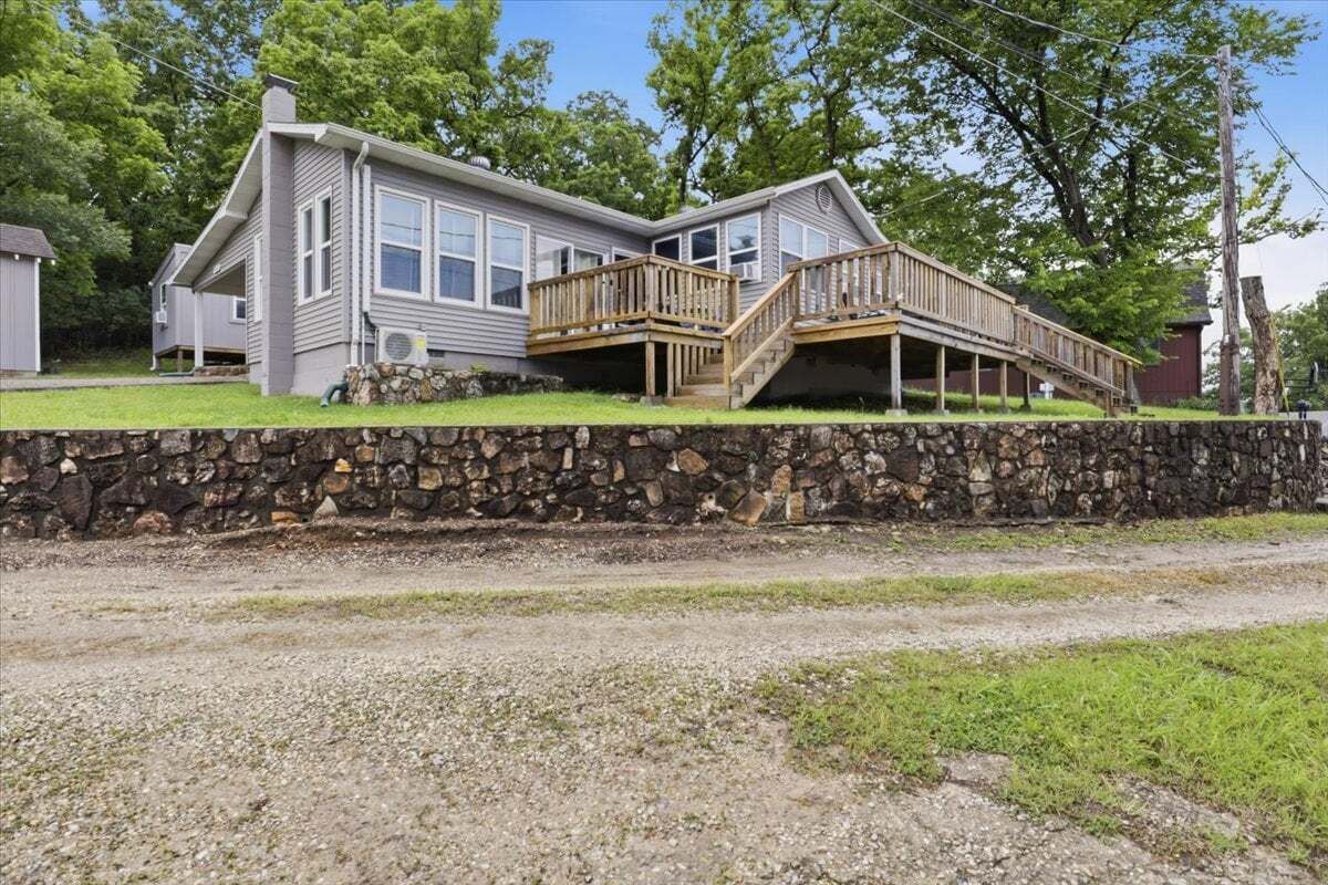 A two-story house with a stone wall foundation, a wooden deck, and a covered porch.