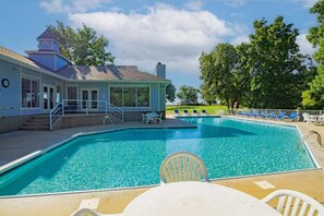 A swimming pool with lounge chairs and a covered area, surrounded by trees and a building with a tower. - Top Floor Lake Views, Loft Space & Private Deck Retreat at the 12mm (Lake Ozark)