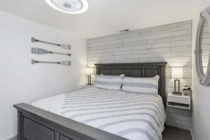 Un dormitorio con una cama, dos mesitas de noche, un espejo en la pared y un ventilador de techo.