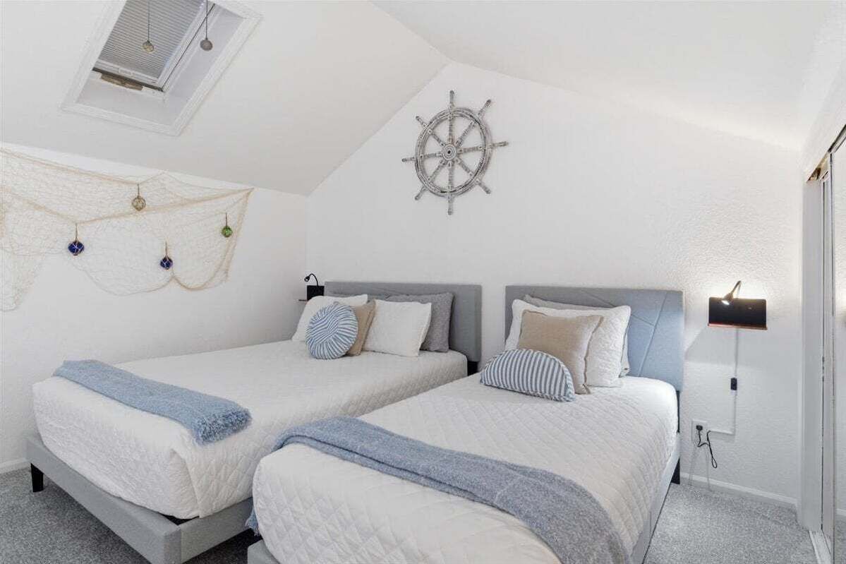 A bedroom with two beds, a ceiling fan, a wall-mounted light, and a decorative wall piece.