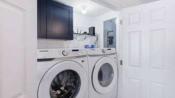 Un área de lavandería con dos lavadoras Samsung blancas, un mueble oscuro y una puerta blanca.