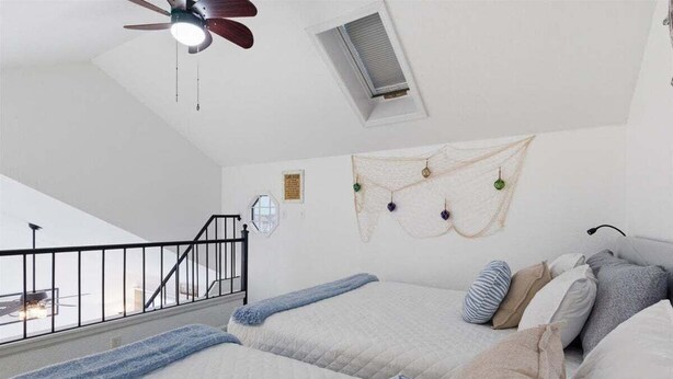 A bedroom with two beds, a ceiling fan, a window, and a staircase.