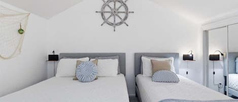 A bedroom with two beds, a ship's wheel decoration, and a small hanging decoration.