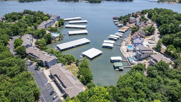 Vue aérienne d’une propriété située au bord de l’eau, comprenant plusieurs quais pour bateaux, un parking et des immeubles résidentiels.