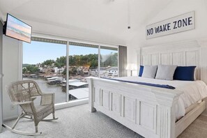 A bedroom with a bed, a chair, a TV, and a view of a waterfront. - Top Floor Lake Views, Loft Space & Private Deck Retreat at the 12mm (Lake Ozark)
