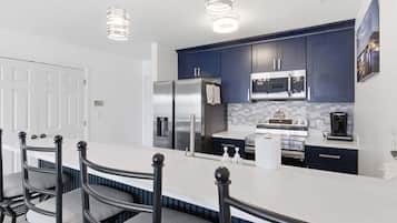 Una cocina moderna con armarios oscuros, electrodomésticos de acero inoxidable y encimera blanca.