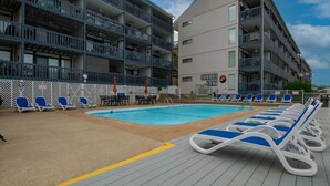 Ein Poolbereich mit Liegestühlen und einem Schwimmbecken, umgeben von mehrstöckigen Gebäuden mit Balkonen.