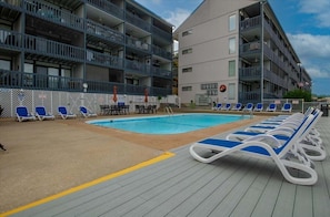 A poolside area with lounge chairs and a swimming pool, surrounded by multi-story buildings with balconies.