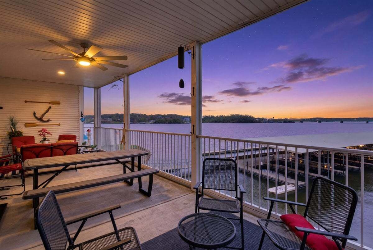 An outdoor deck with a view of a body of water, a ceiling fan, and seating arrangements.
