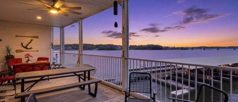 An outdoor deck with a view of a body of water, a ceiling fan, and seating arrangements.