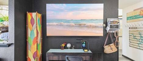Une pièce comprenant un bureau, une chaise et un grand tableau représentant une scène de plage.
