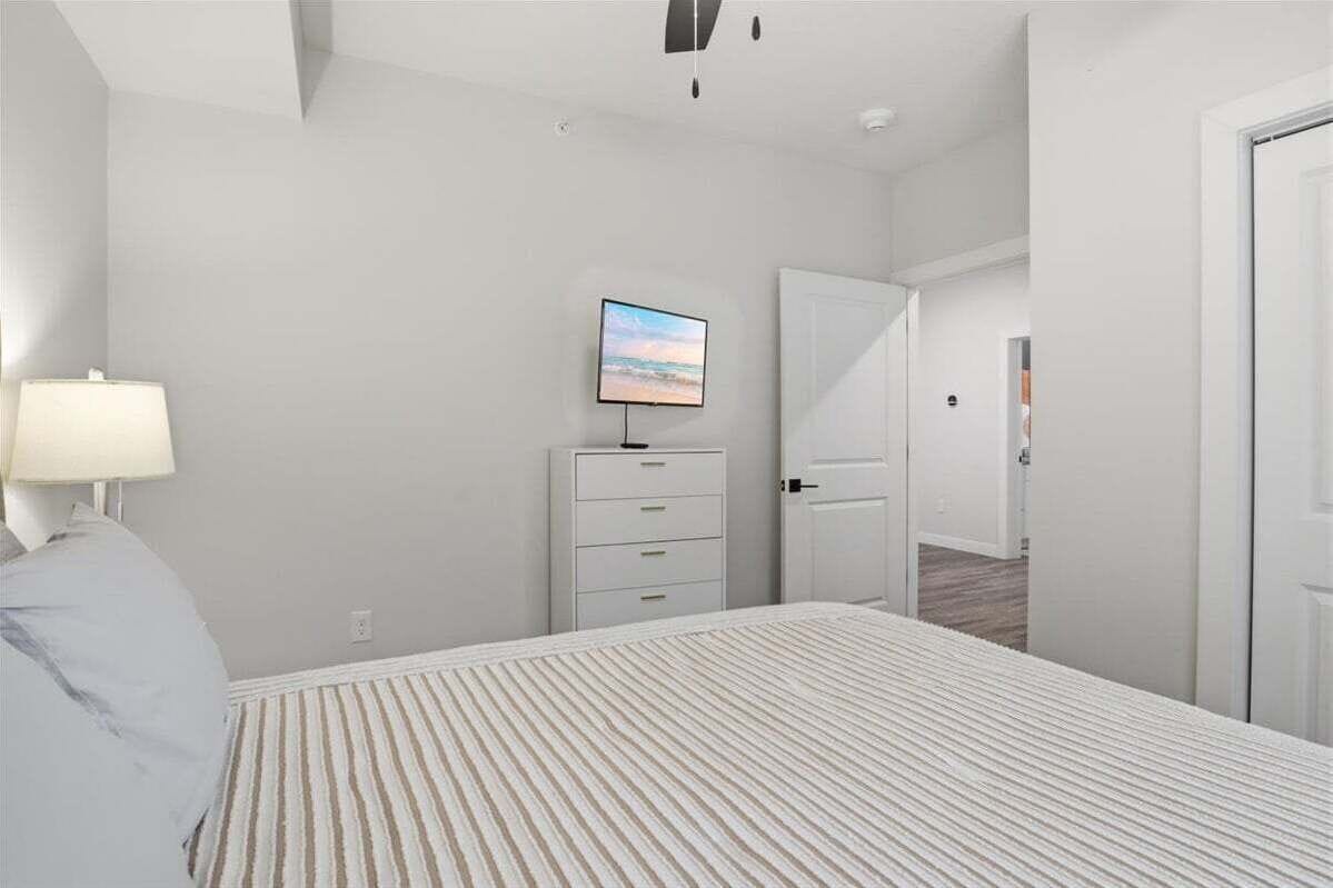 A bedroom with a bed, a TV on a dresser, a door, and a hallway.