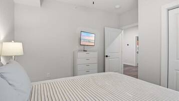 A bedroom with a bed, a TV on a dresser, a door, and a hallway.