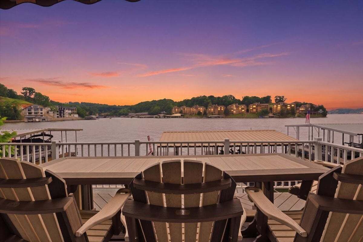 A waterfront deck with wooden tables and chairs, overlooking a body of water and a row of buildings.