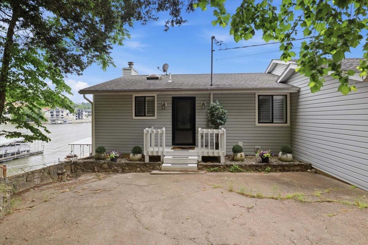 A single-story house with a front porch, a satellite dish, and a small garden with potted plants.