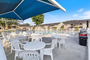 An outdoor pool area with white plastic chairs and tables, a blue umbrella, and a clear sky. - Lakefront Condo With Boat Slip, Heated Pool & Boat Launch (Osage Beach)