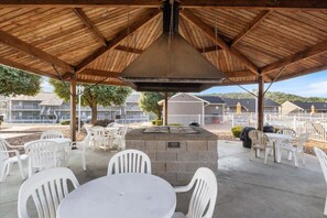 An outdoor patio area with a stone table and white plastic chairs, surrounded by a wooden pergola structure. - Lakefront Condo With Boat Slip, Heated Pool & Boat Launch (Osage Beach)