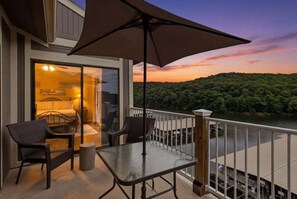 An outdoor balcony with a glass door leading to a room, a table, chairs, and a large umbrella. - Lakefront Condo With Boat Slip, Heated Pool & Boat Launch (Osage Beach)