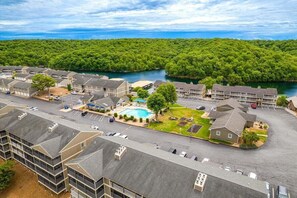 A hotel with a swimming pool, parking lot, and a view of a river and forest. - Lakefront Condo With Boat Slip, Heated Pool & Boat Launch (Osage Beach)