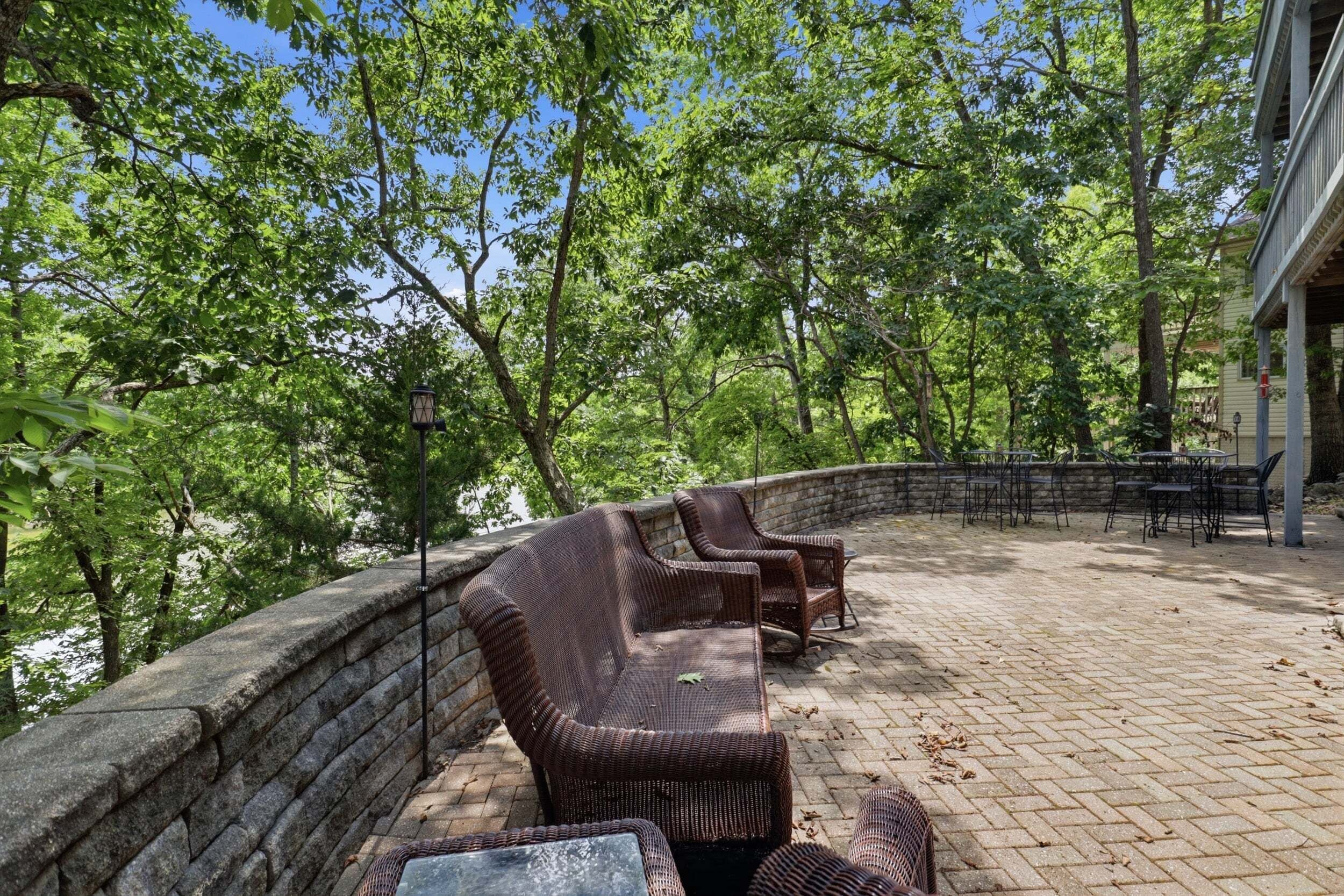 An outdoor patio with wicker furniture, a stone wall, and a view of trees.