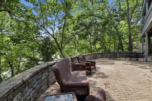 Eine Terrasse im Freien mit Korbmöbeln, einer Steinmauer und Blick auf Bäume.