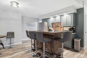 A kitchen with bar stools, a refrigerator, and a coffee machine. - Lakefront Near Party Cove w/ Dock, Kayaks, Bunk Room & Multi-level Decks (Osage Beach)