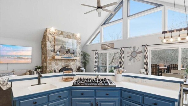 A kitchen with blue cabinets, a stone backsplash, a gas stove, and a ceiling fan. - Lakefront Near Party Cove w/ Dock, Kayaks, Bunk Room & Multi-level Decks (Osage Beach)