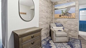 A room with a wooden dresser, a round mirror, a gray armchair, a patterned rug, and a painting of a dock. - Lakefront Near Party Cove w/ Dock, Kayaks, Bunk Room & Multi-level Decks (Osage Beach)