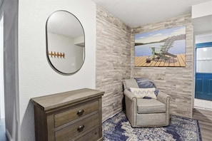 A room with a wooden dresser, a round mirror, a gray armchair, a patterned rug, and a painting of a dock. - Lakefront Near Party Cove w/ Dock, Kayaks, Bunk Room & Multi-level Decks (Osage Beach)