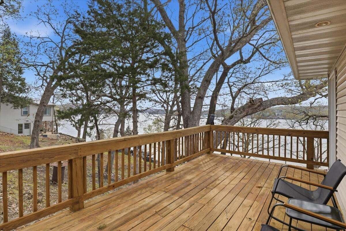 Une terrasse en bois avec une rambarde, une chaise et une vue sur les arbres et un paysage lointain.