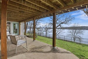 An outdoor covered patio with a table and chairs, overlooking a body of water and a fenced area.
