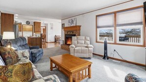 Una sala de estar con chimenea, un sofá, una mesa de centro y vistas al exterior a través de grandes ventanales.