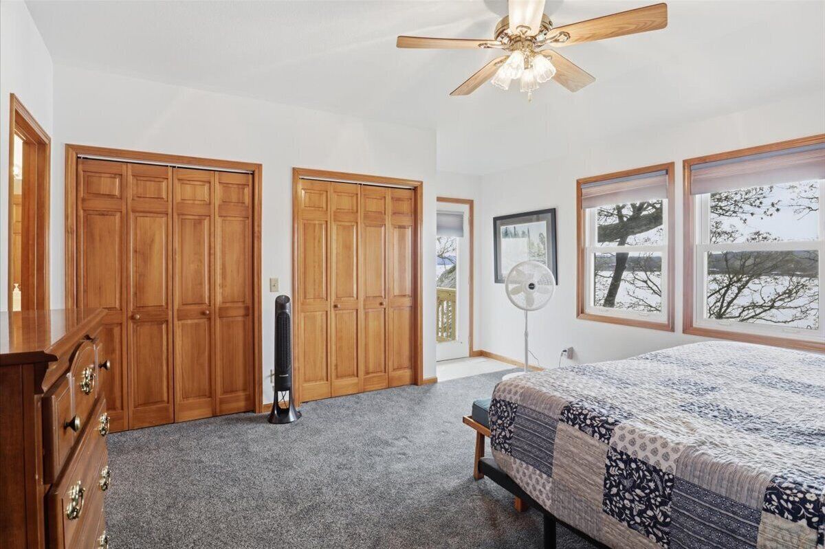 A bedroom with a bed, wooden wardrobe, ceiling fan, and a window with a view.