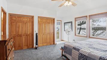 A bedroom with a bed, wooden wardrobe, ceiling fan, and a window with a view.
