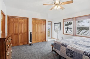 A bedroom with a bed, wooden wardrobe, ceiling fan, and a window with a view.