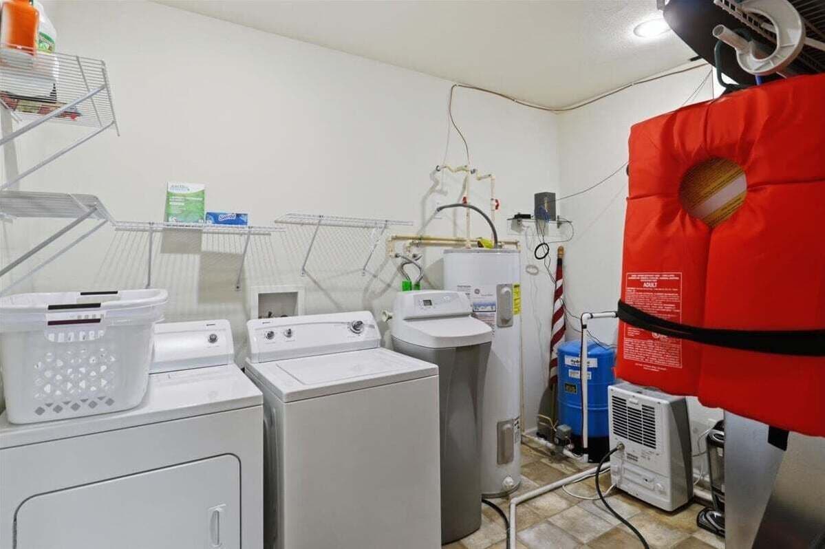Une buanderie équipée de machines à laver et de sèche-linge, d’un chauffe-eau et d’un panneau de signalisation rouge indiquant les consignes de sécurité.