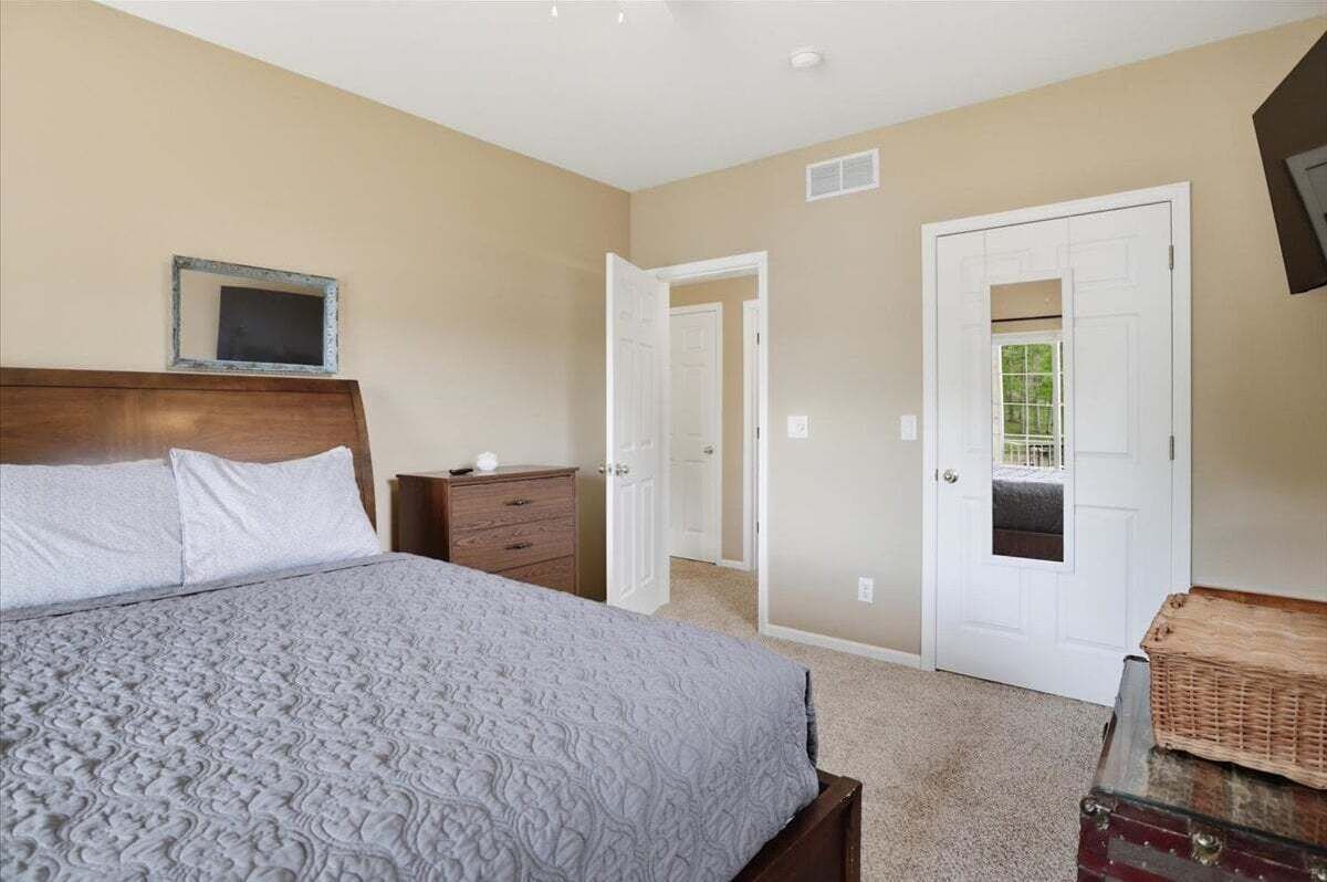 A bedroom with a bed, dresser, and a door leading to another room.