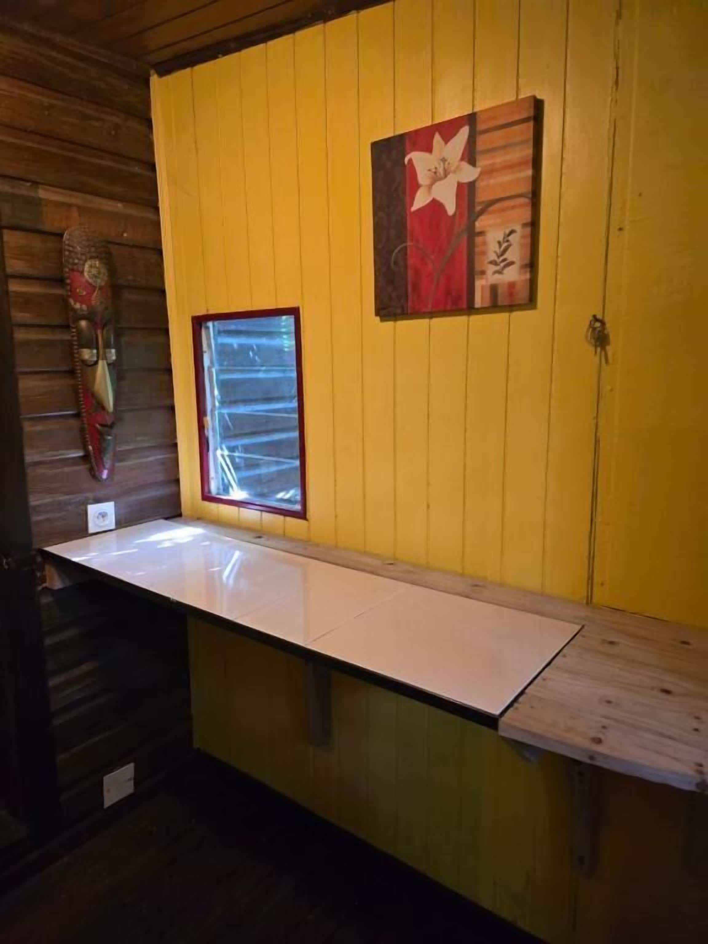A room with a wooden ceiling, a yellow wall, a window with blinds, and a white counter.