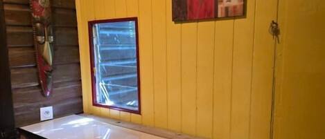 A room with a wooden ceiling, a yellow wall, a window with blinds, and a white counter.