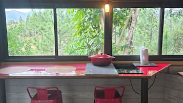 A kitchen with a large window, two red stools, a red pot on the counter, and a paper towel dispenser.