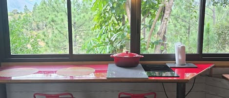 Una cocina con un ventanal amplio, dos taburetes rojos, una olla roja sobre la encimera y un dispensador de toallas de papel.
