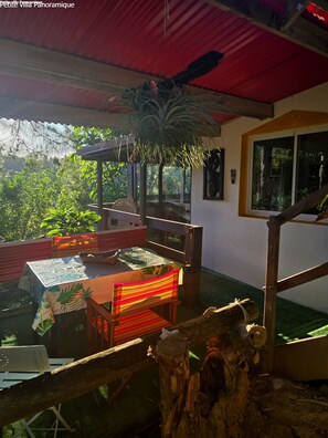 Un patio exterior con mesa y sillas, una planta colgante y vistas al verdor.