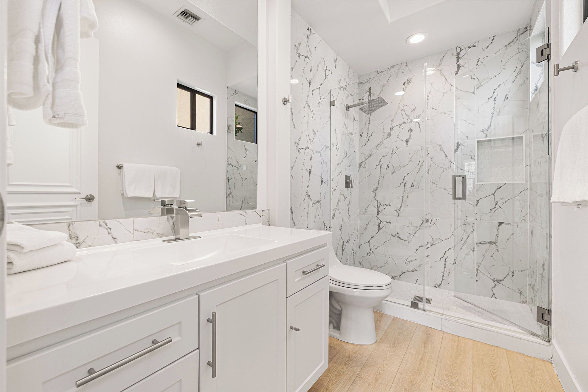 A modern bathroom with a marble shower, a toilet, and a vanity with a sink and mirror.