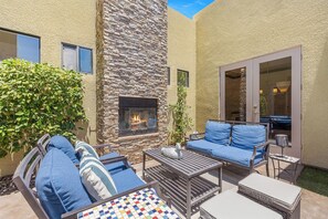 An outdoor patio with a stone fireplace, blue cushioned seating, and a small table. - Casa Sonora Grande - A Palm Springs 6 bedroom gem! (Palm Springs)