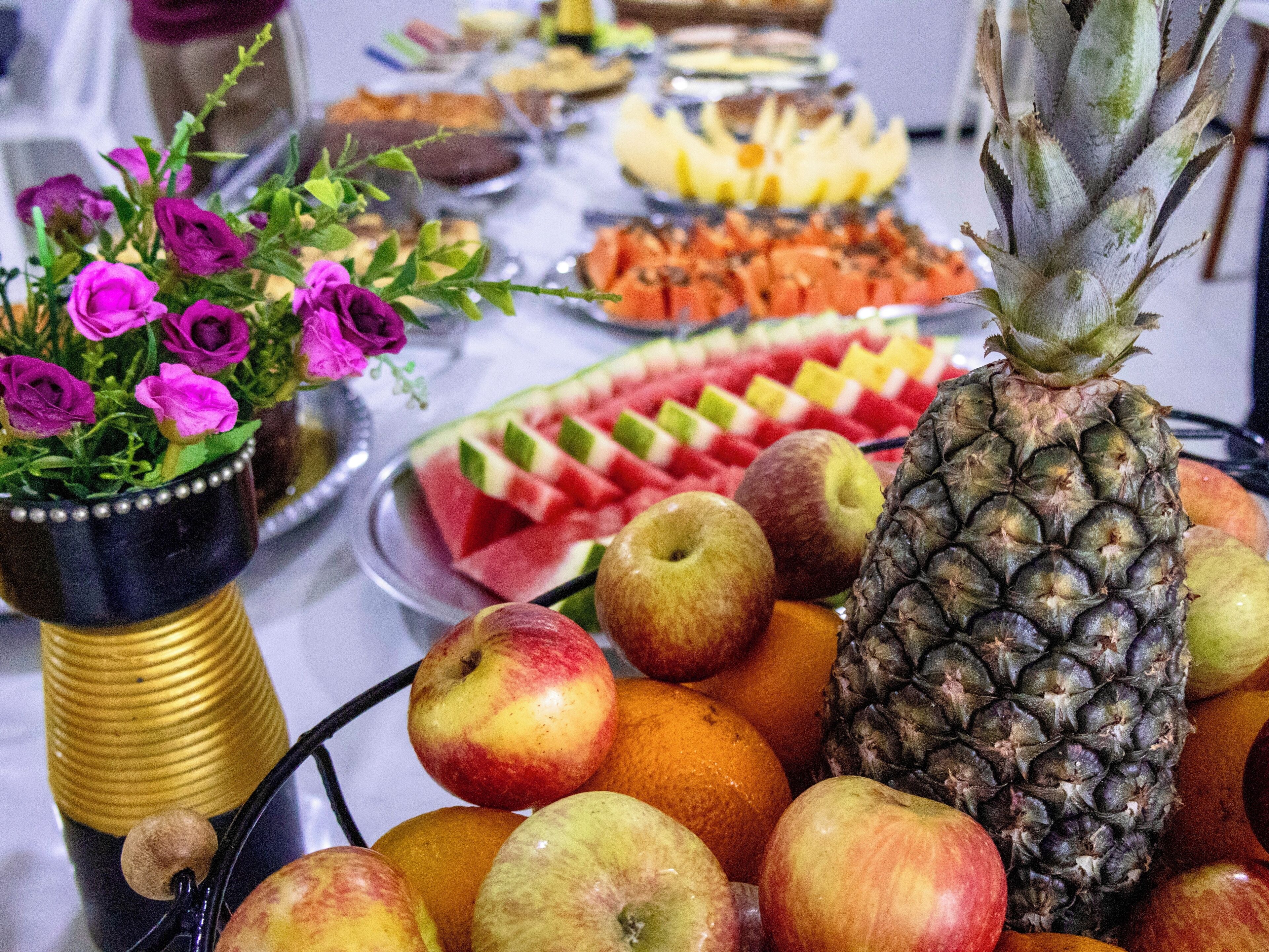 Una mesa de buffet con diversas frutas y un centro de mesa floral.