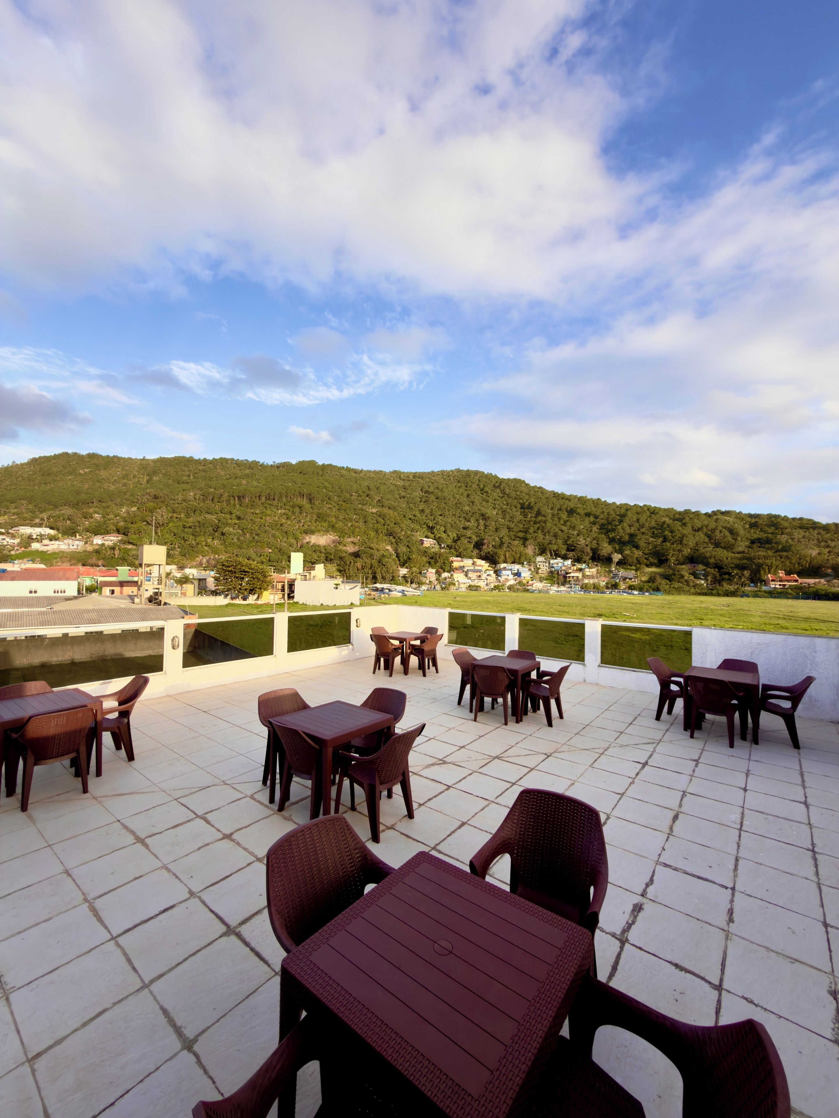 Eine Terrasse im Freien mit Tischen und Stühlen, mit Blick auf eine grüne Landschaft und einen Hügel.