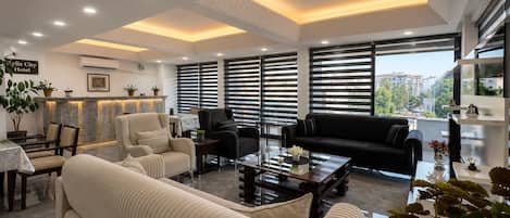 A modern hotel lobby with a sofa, armchairs, a coffee table, and a reception desk.