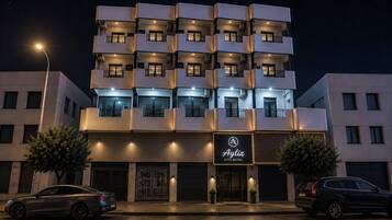 A multi-story hotel with balconies, a sign reading 'Ayliz City Hotel,' and two cars parked in front.